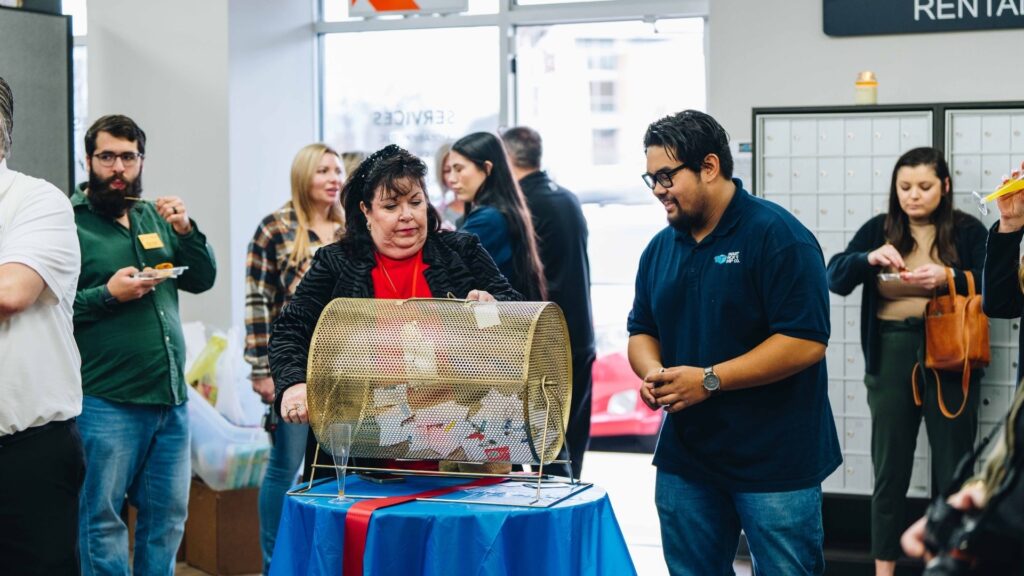Crowd gathered around a raffle drum at a retail store grand opening event, celebrating a new business.