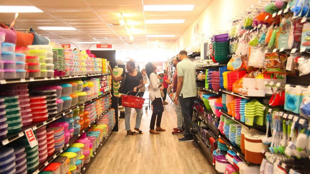 Customers shopping in a brightly lit dollar store aisle filled with colorful plastic storage containers and kitchenware.